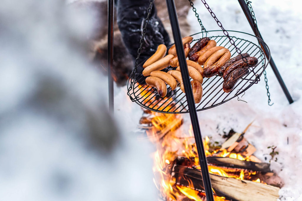 Barbecue d'hiver @Flarken Adventure Les saucisses cuisent au feu de bois en Laponie suédoise