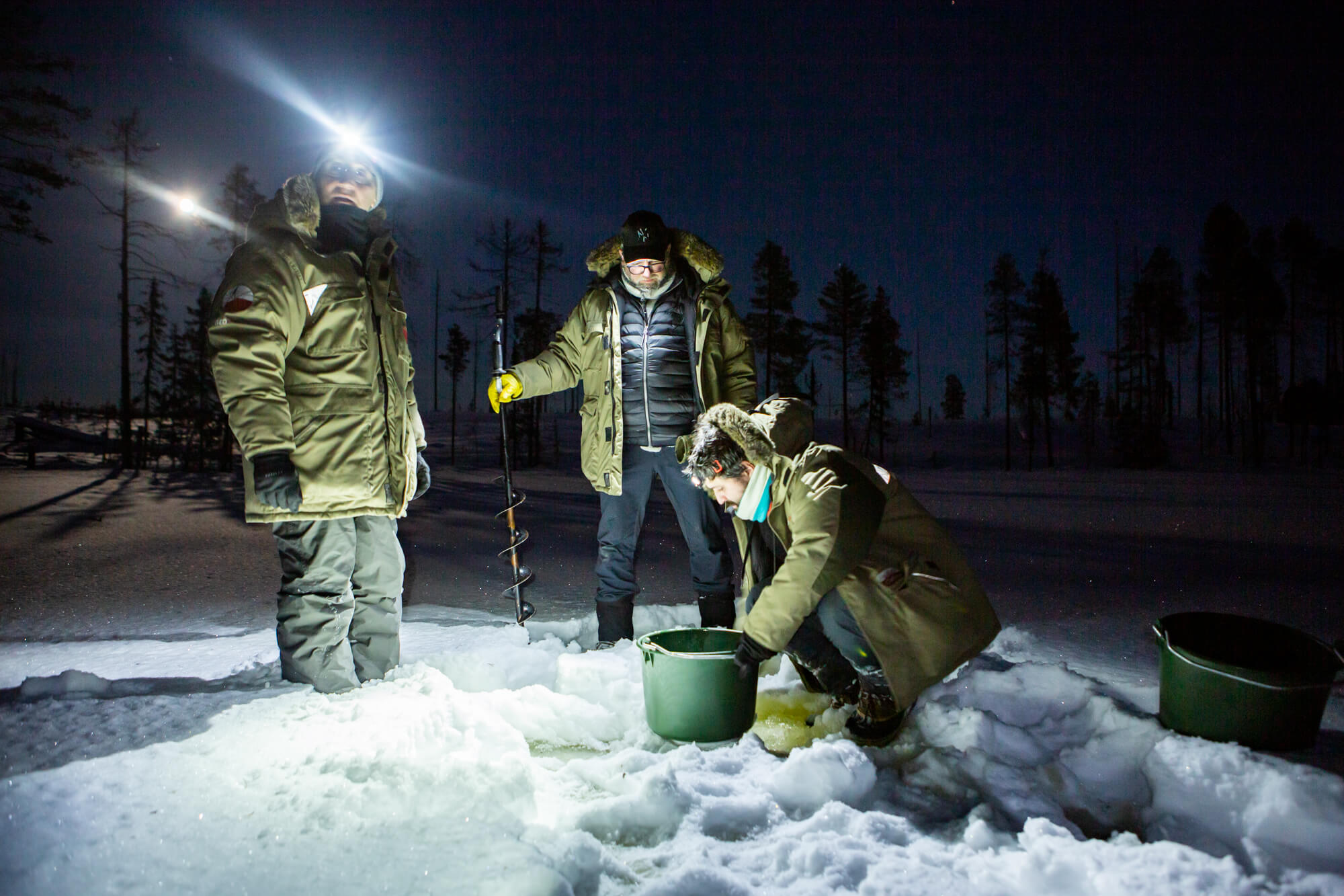 3 hommes puisent de l'eau dans un lac gelé en laponie suédoise