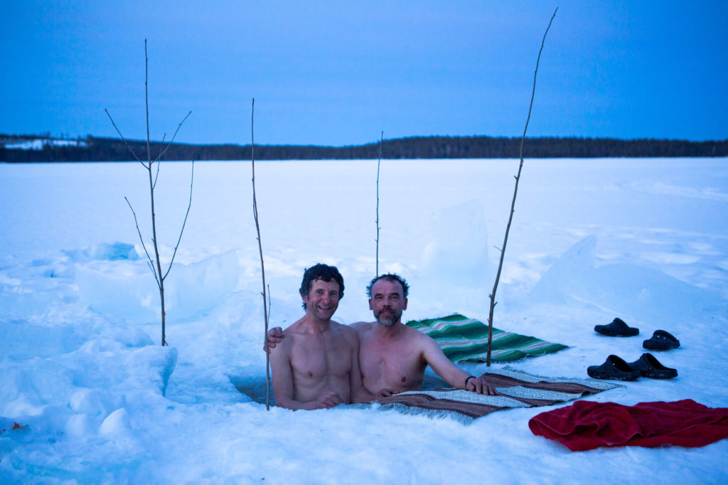 Deux hommes se rafraichissent dans un trou de glace après un sauna en Laponie suédoise
