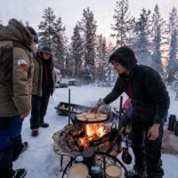 avis-voyageurs-suede-laponie-flarken-adventure-262 Quatre personnes autour d'un feu sur un campement en hiver en laponie @Flarken Adventure